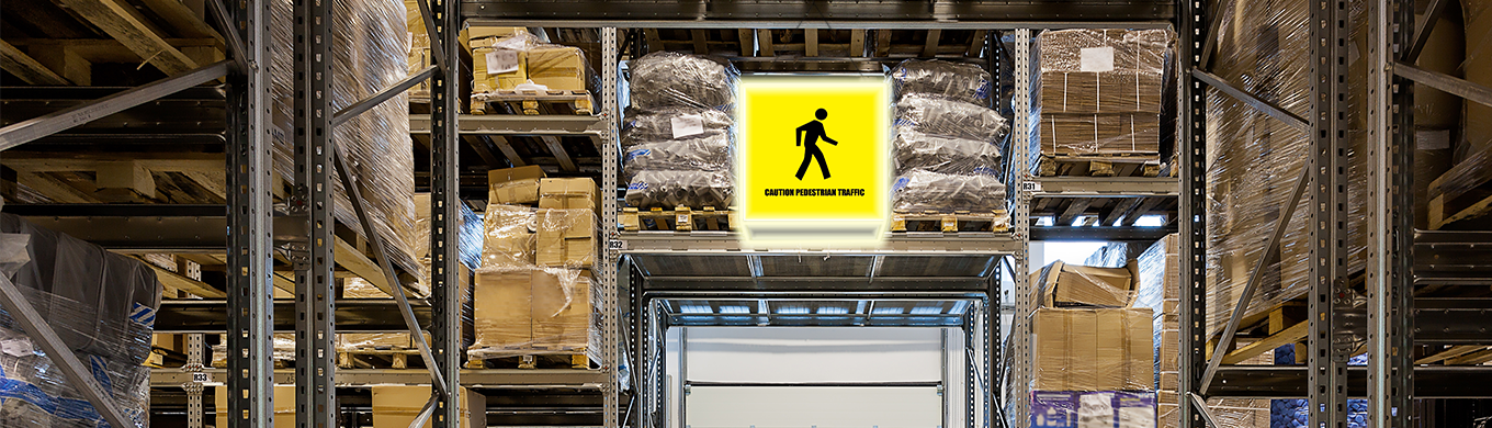 Close-up van een geel verlicht LED-waarschuwingsbord met voetgangerspictogram en de tekst "Caution Pedestrian Traffic", bevestigd aan een magazijnrek / Gros plan d'un panneau d'avertissement LED jaune lumineux avec pictogramme piéton et le texte "Caution Pedestrian Traffic", fixé à un rayonnage d'entrepôt