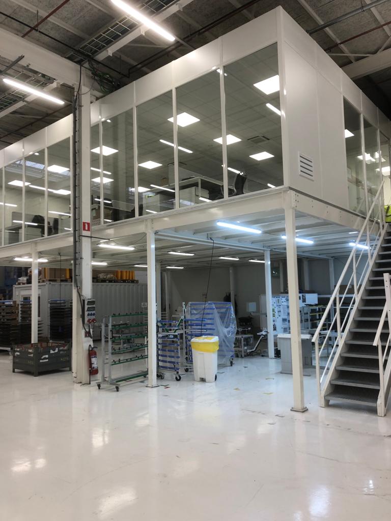 Stalen mezzanine met open begane grond, afgesloten bovenverdieping en stalen trap in een productiehal