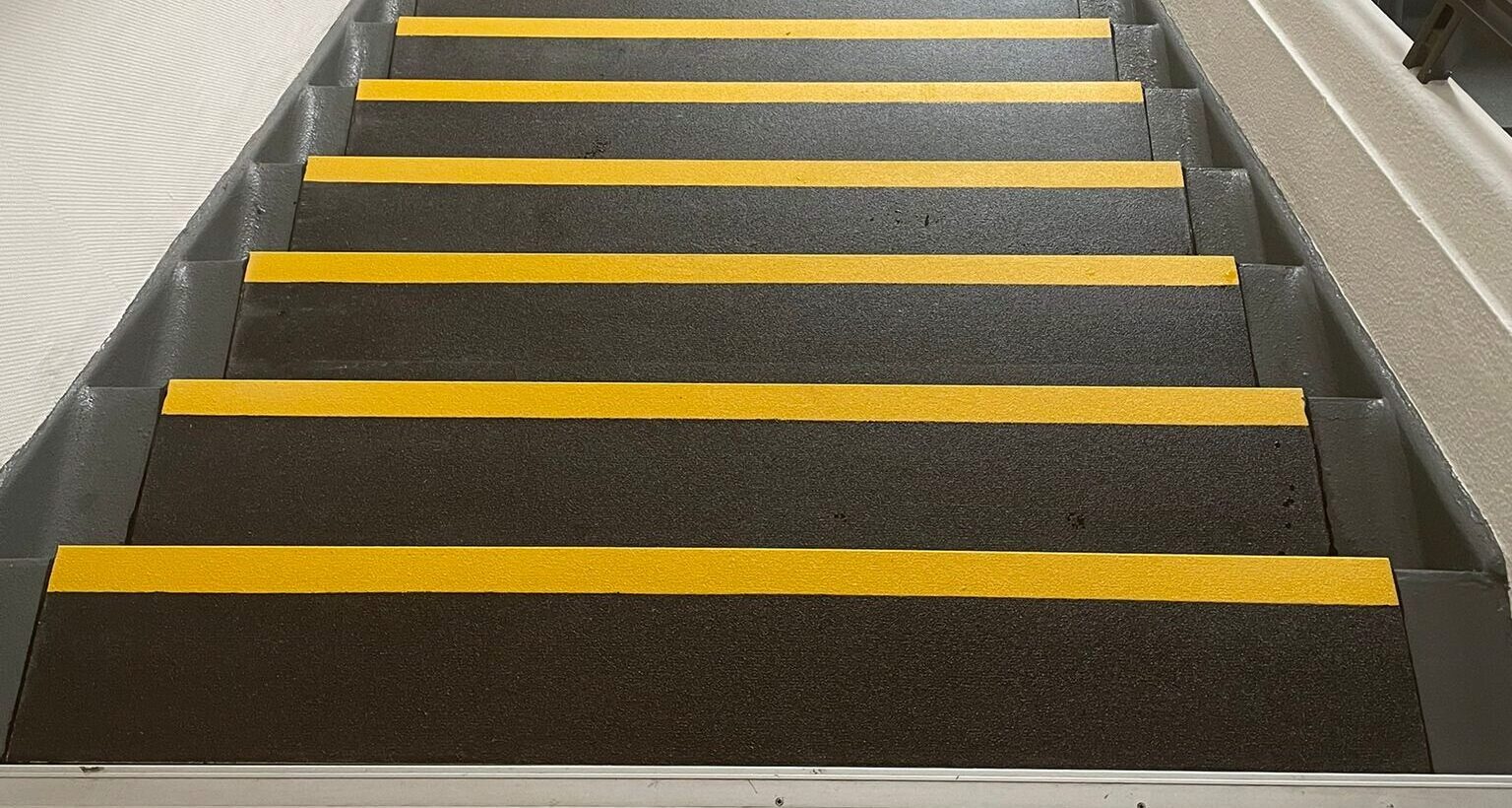 Binnentrap met gele antislip GRP trapneuzen op donkere traptredes in een industriële omgeving.