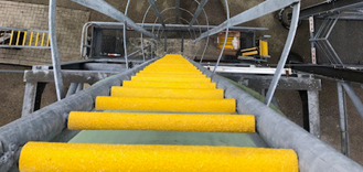 Bovenaanzicht van een steile industriële trap met gele GRP antislip trapprofielen op elke trede, omgeven door een stalen kokerbeveiliging