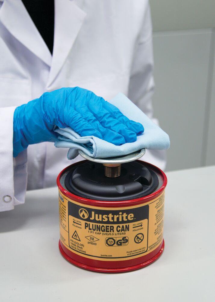 Laboratoriummedewerker met blauwe handschoenen die een rode Justrite Plunger Can gebruikt voor het doseren van ontvlambare vloeistoffen