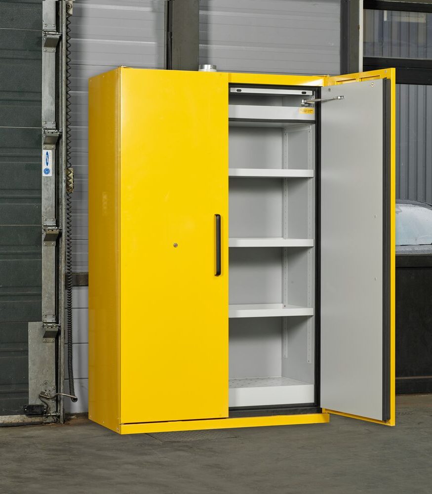Gele brandveilige veiligheidskast met één open deur en drie lege verstelbare schappen, opgesteld buiten voor een industrieel gebouw.