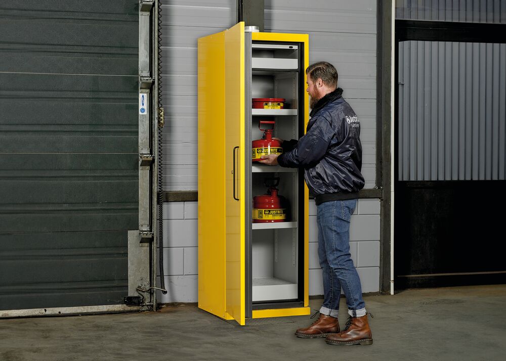 Man plaatst rode Justrite veiligheidskannen in een gele brandveilige kast in een industriële hal.