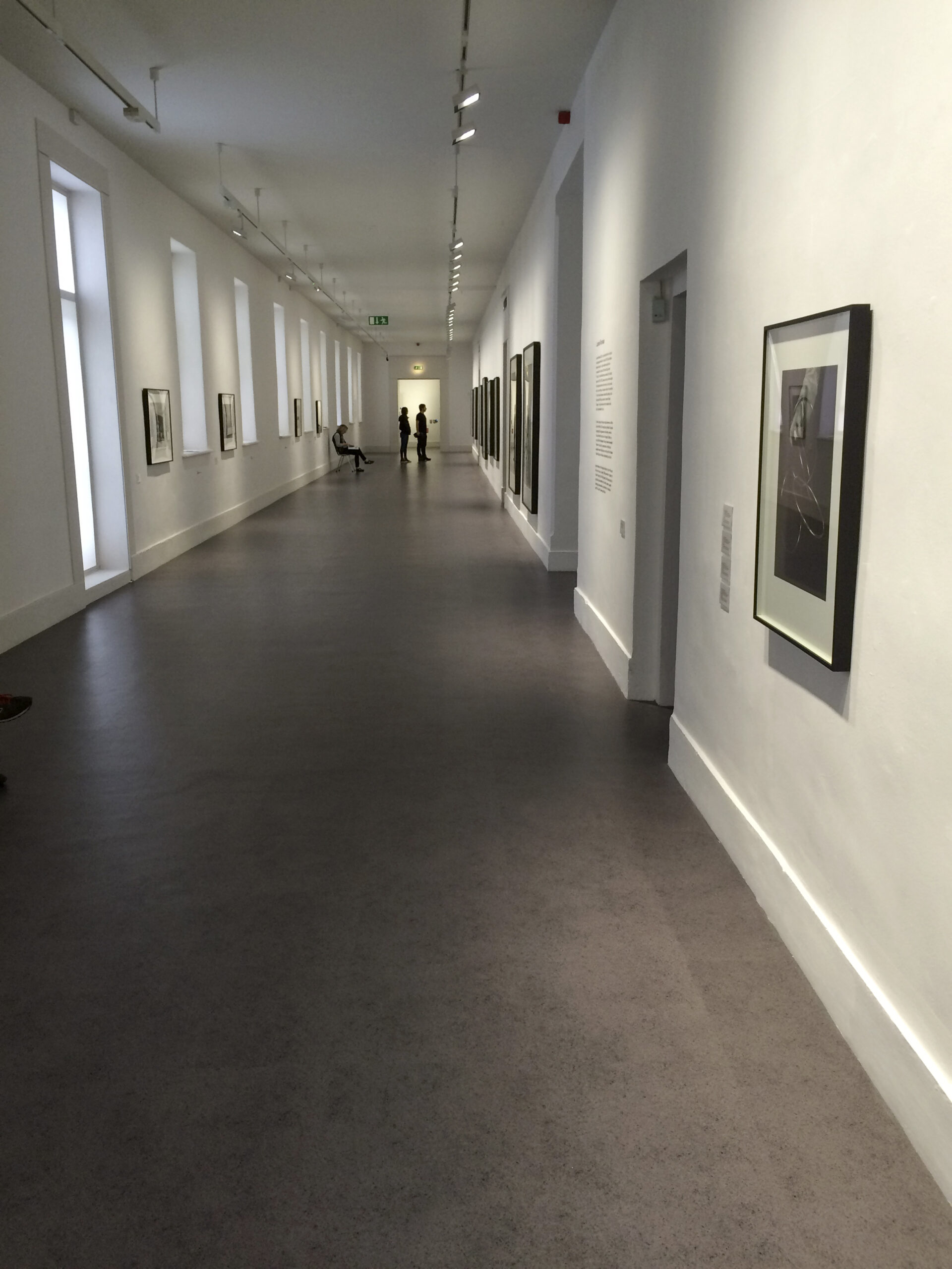 Lange museumgang met grijze commerciële vinyl vloer in steeneffect door AWP
