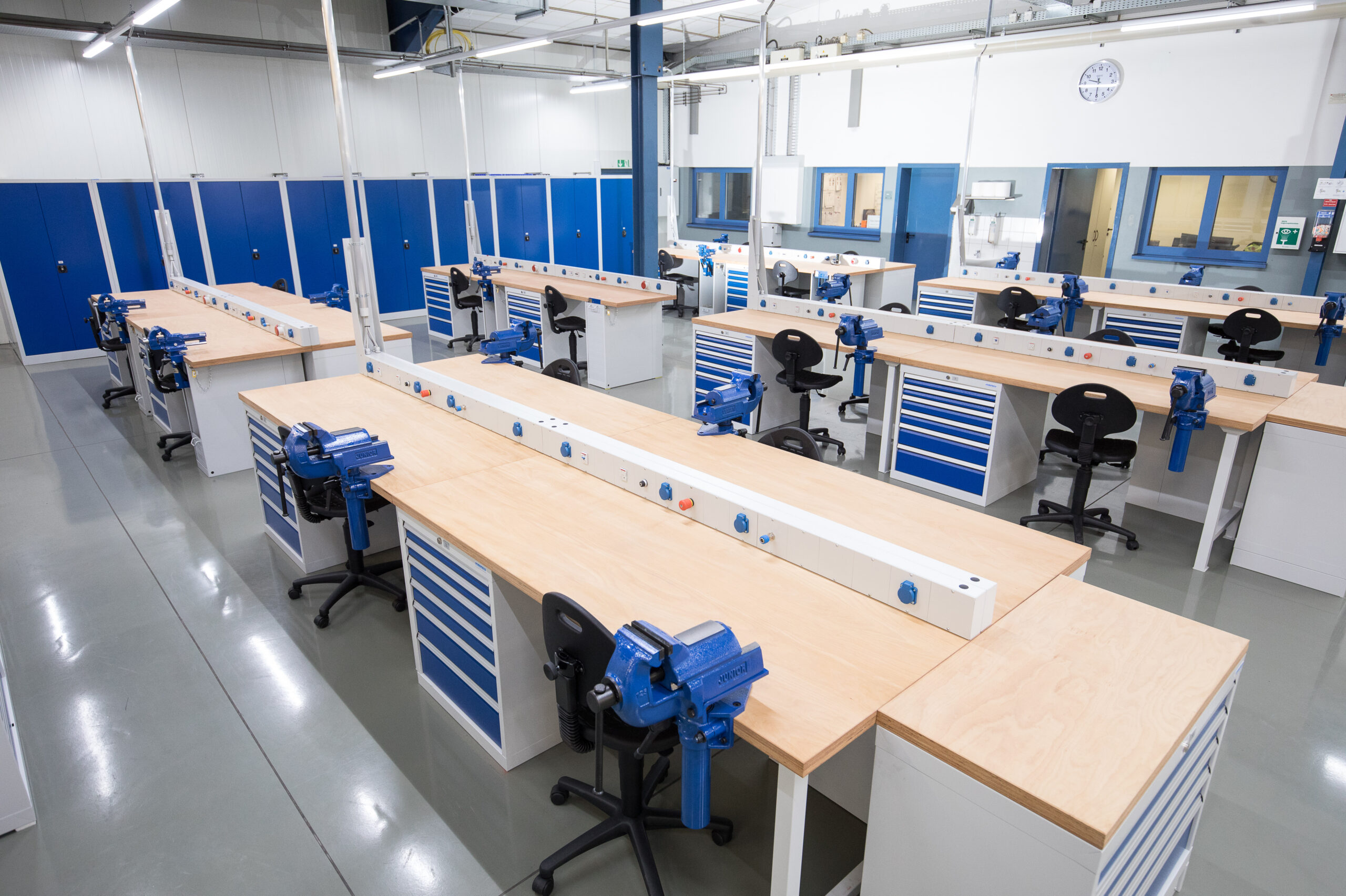 Rij professionele werktafels met blauwe bankschoreven, ladekasten en ergonomische stoelen in een moderne werkplaats