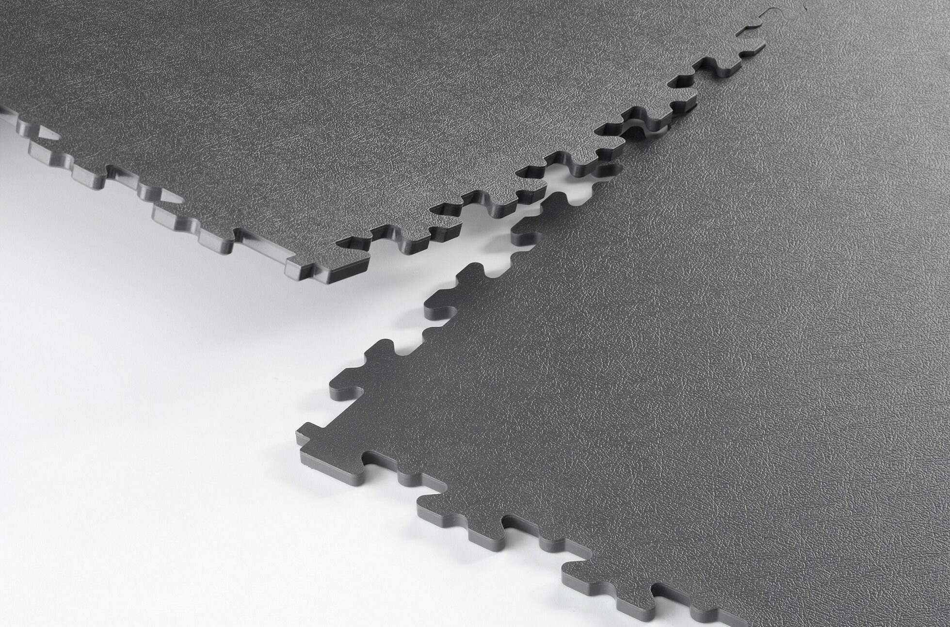 Donkergrijze ESD-vloertegels met puzzelvormige X-verbindingen die naadloos in elkaar passen, ontworpen voor de aanleg van een geleidende vloer in elektrostatisch gevoelige werkomgevingen. Dalles de sol ESD gris foncé dotées de raccords en X en forme de puzzle qui s'emboîtent parfaitement, conçues pour la pose d'un sol conducteur dans les environnements de travail sensibles aux décharges électrostatiques.