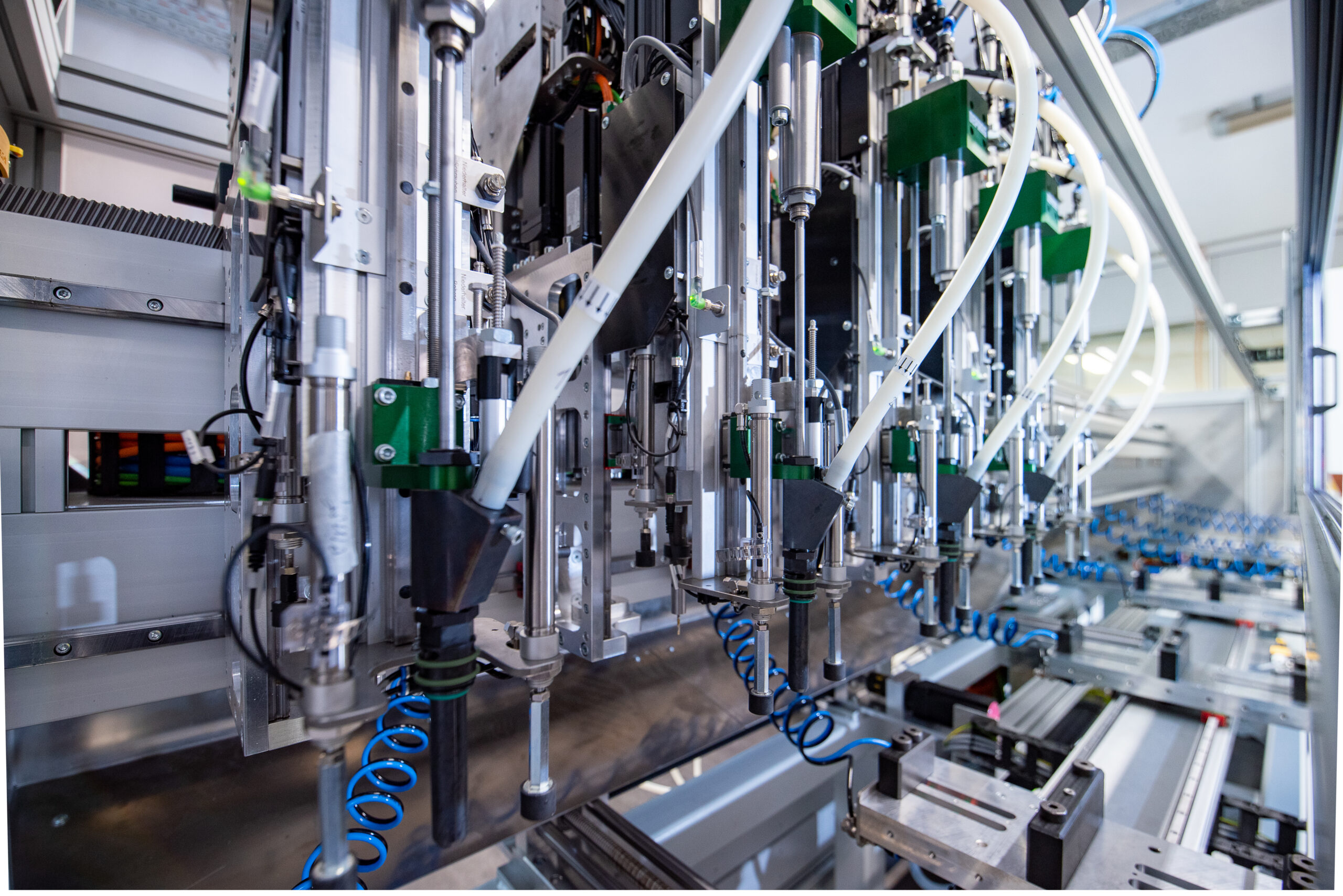 Close-up van een industriële geautomatiseerde schroefmachine met meerdere verticale Deprag schroefeenheden, blauwe persluchtslangen en witte toevoerbuizen in een productieomgeving.