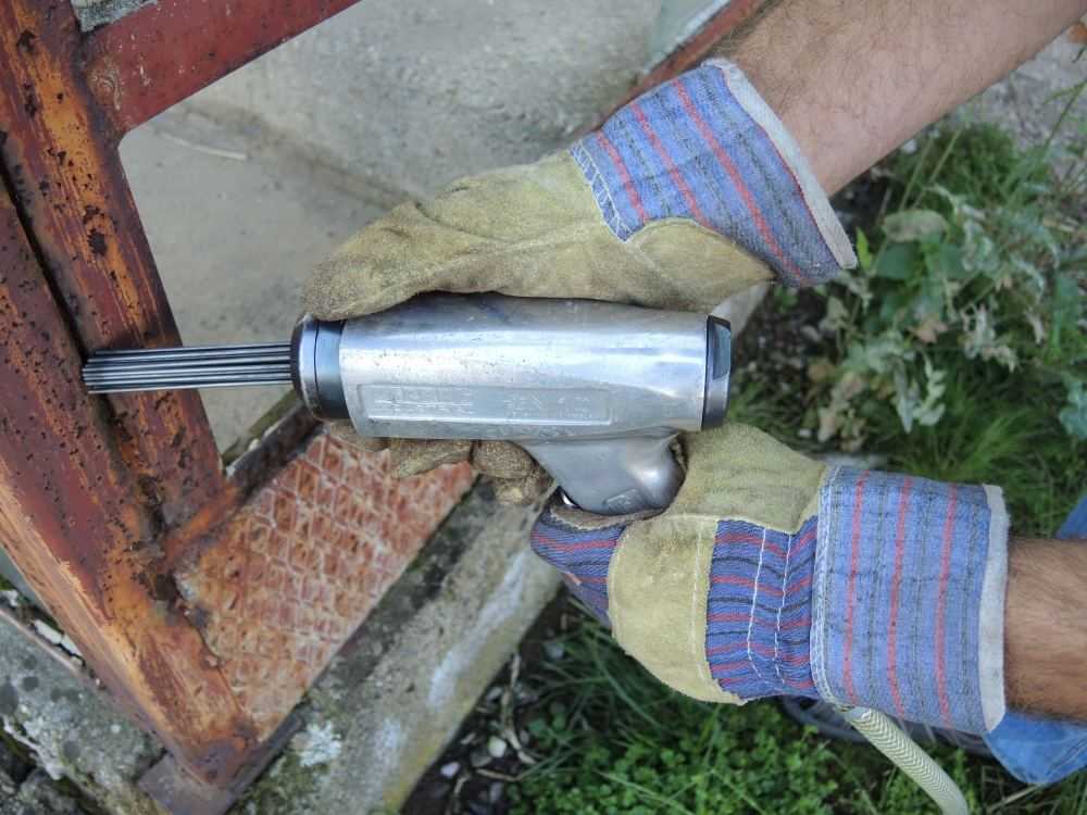 Pneumatische naaldbikhamer met pistoolgreep bij het verwijderen van roest op een metalen constructie — AWP