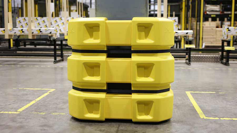 Gele modulaire kolombeveiliging opgebouwd uit gestapelde polyethyleen segmenten met zwarte banden, geplaatst voor een kolom in een industriële productiehal