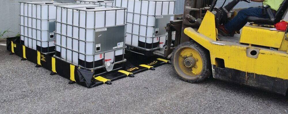 Heftruck die IBC-containers plaatst op een zwarte flexibele Justrite opvangbak met gele inrijrand buiten