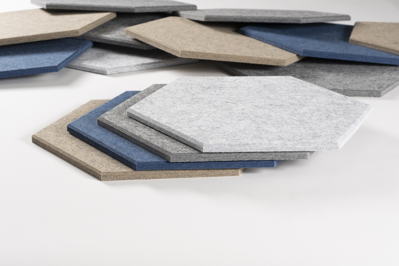 Productfoto van gestapelde akoestische hexagon tegels in lichtgrijs, donkergrijs, blauw en beige