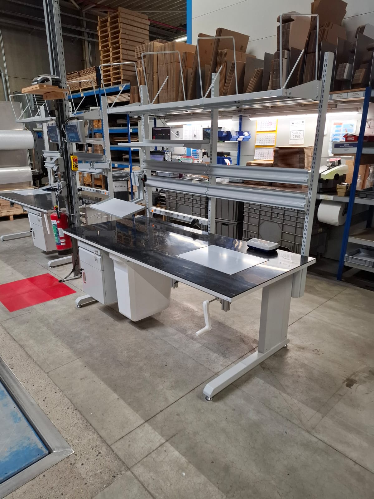 volledig uitgeruste industriële werktafel met zwart werkblad, aluminium bovenstelling met documenthouders en vuilnisbakken onder het blad, opgesteld in het AWP-atelier voor levering