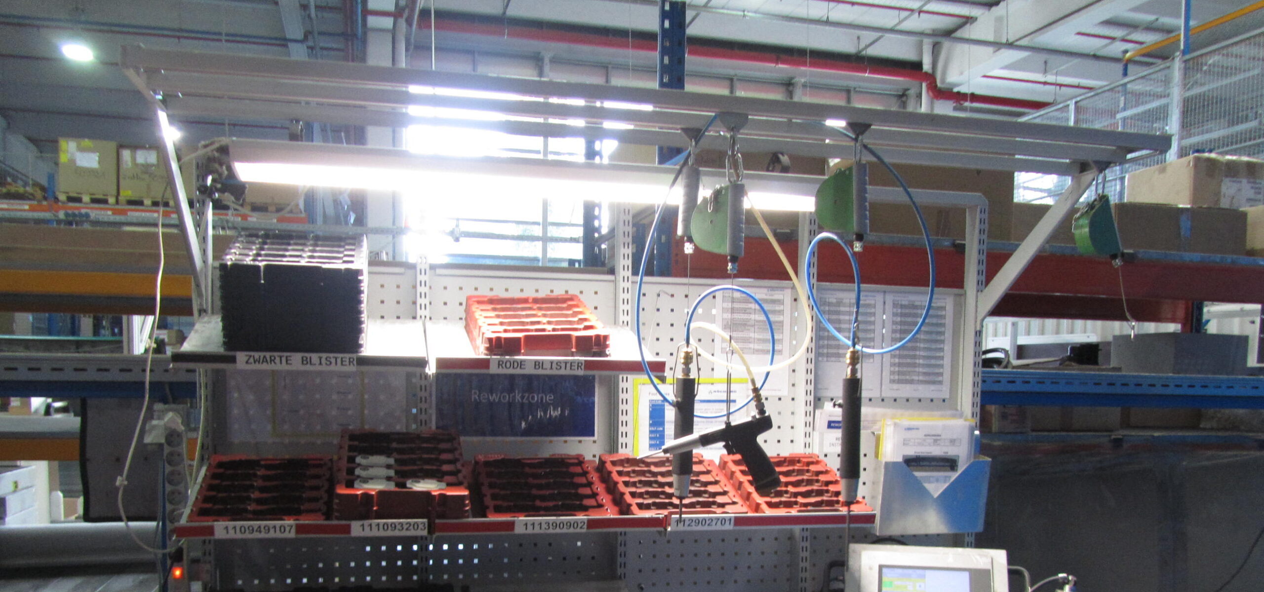 Werkpost in automotive assemblage met pneumatische handschroevendraaiers aan veerbalancers, geperforeerde achterwand, gelabelde componentenbakken en een touchscreenpaneel