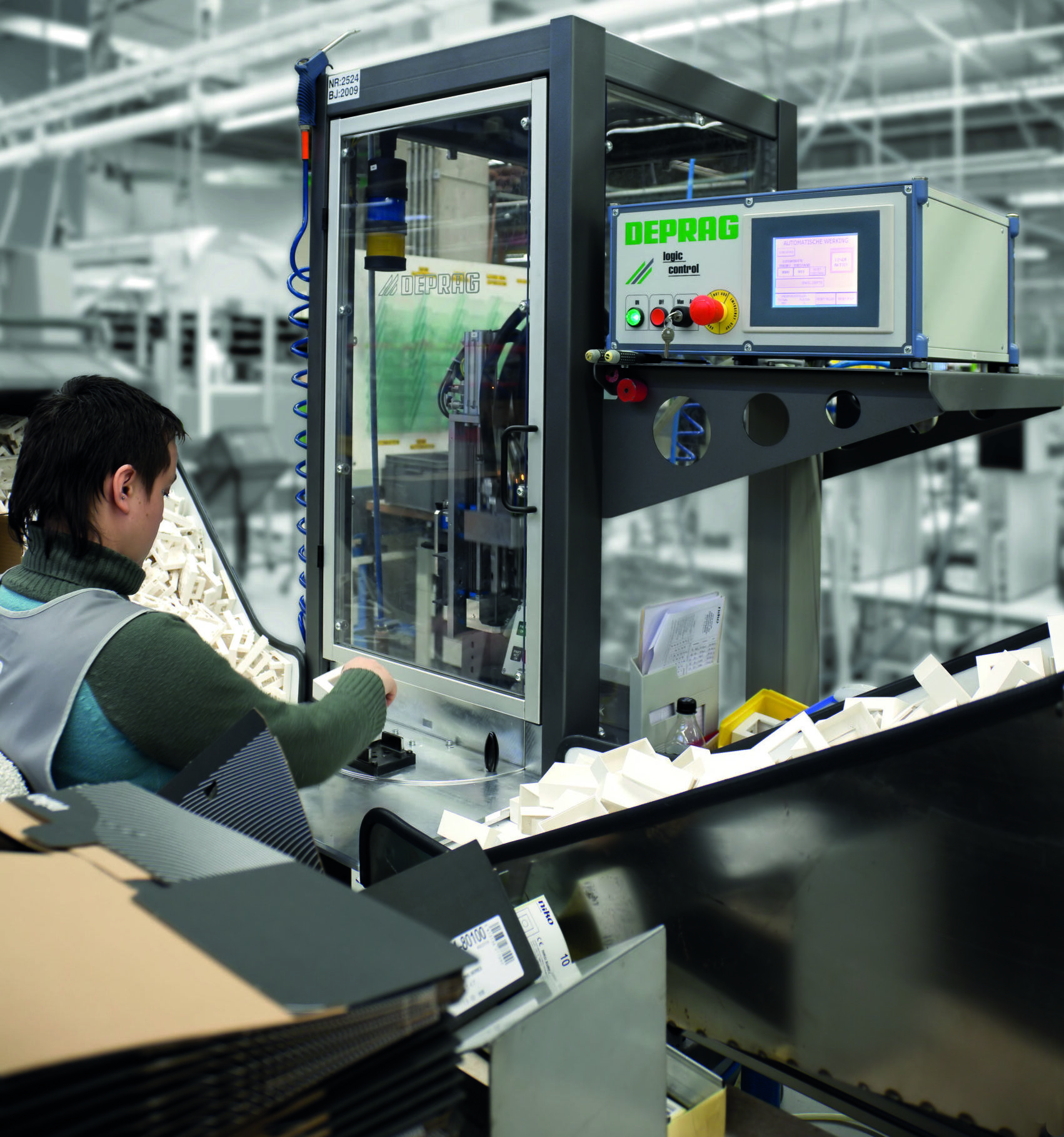 Operator die een kunststof opbouwdoos plaatst in de DEPRAG automatische schroefmachine bij Niko, met de Logic Control besturingskast zichtbaar op de voorgrond