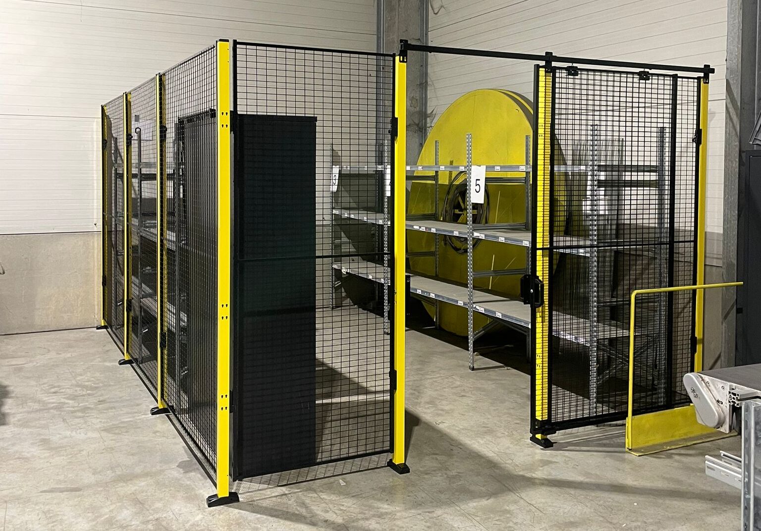 Hekwerkafscheiding met zwart gaaswerk en gele staanders rond een grote gele industriële machine in een productieruimte
