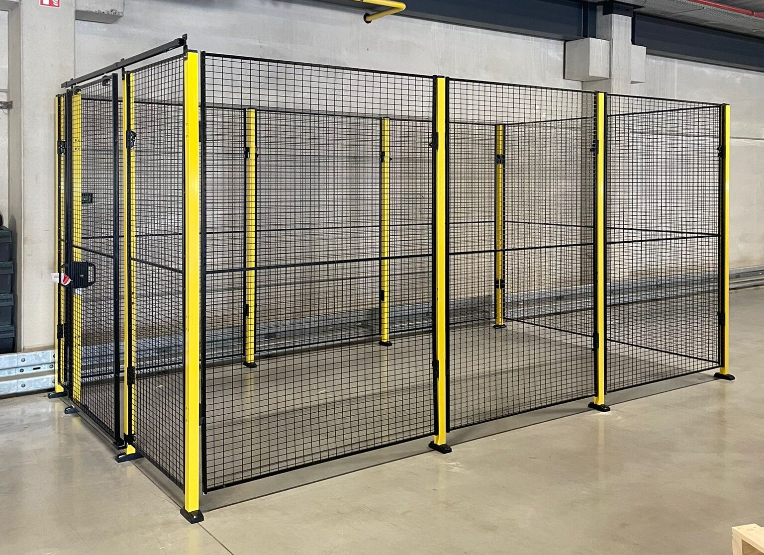 Volledig gesloten rechthoekig hekwerk met zwart gaaswerk en gele staanders op een lichte epoxyvloer in een magazijnruimte