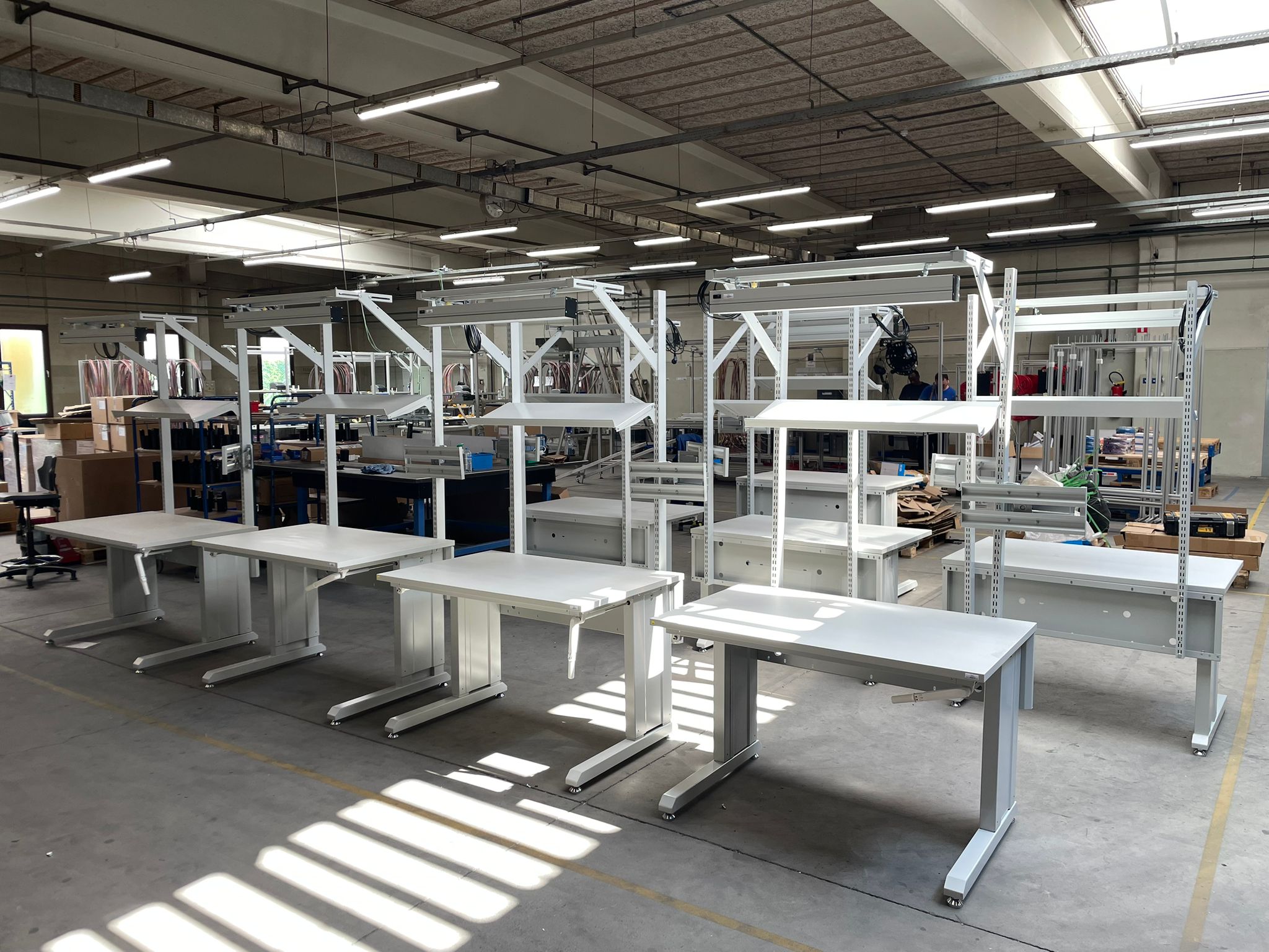 Rij industriële werktafels met LED werkplekverlichting direct gemonteerd op het bovenframe in een grote productiewerkplaats. Werkplaatsinrichting door AWP.