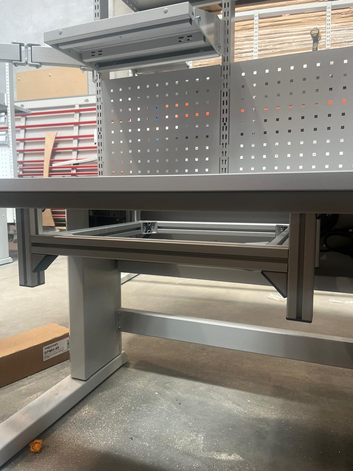 Onderaanzicht van een industriële werktafel met uitschuifbare lade onder het tafelblad en geperforeerde achterwand op de achtergrond