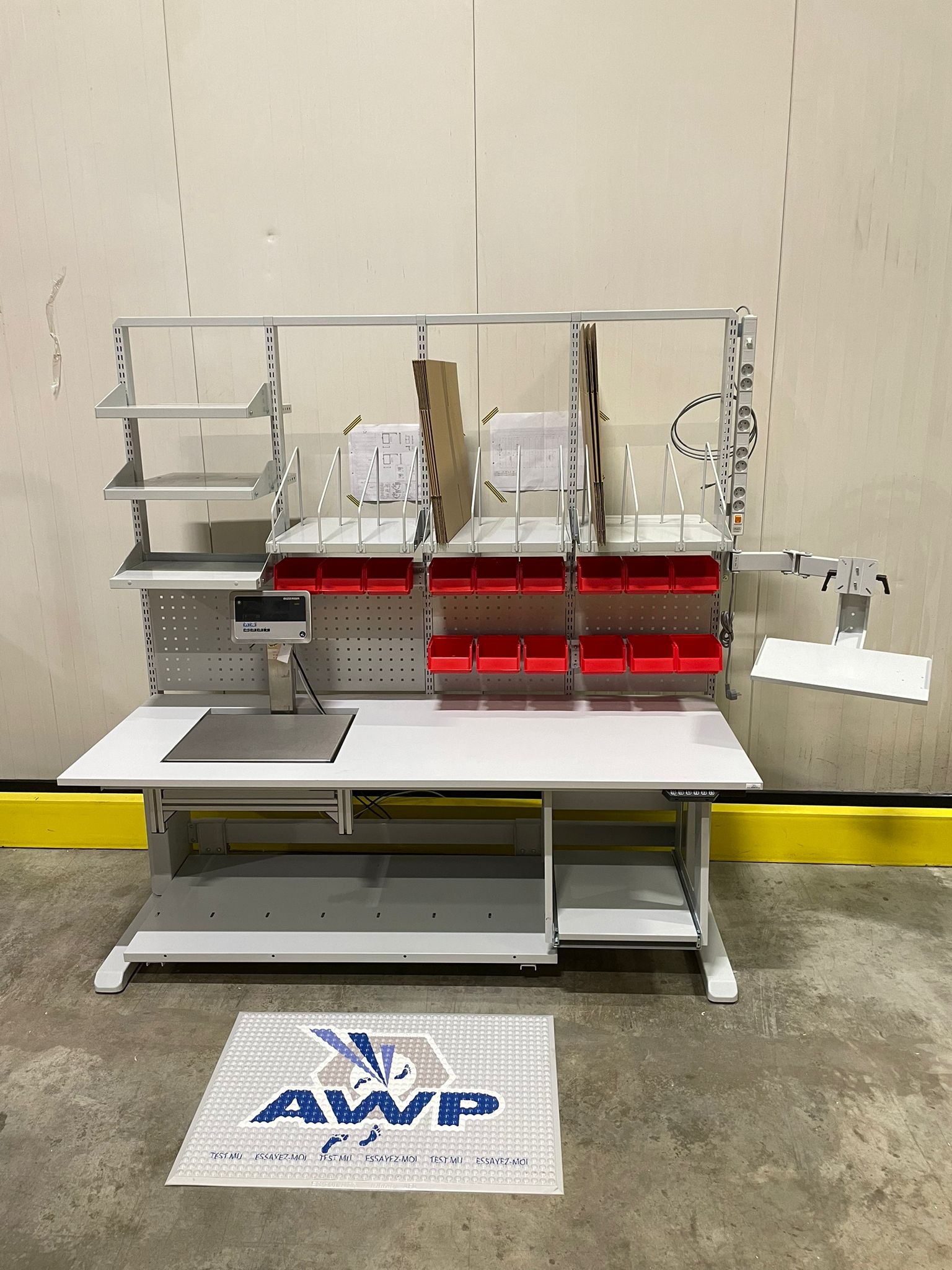 Volledig uitgeruste maatwerk werktafel met geïntegreerde weegschaal, rode grijpbakken, bovenstellingen en monitorarm, met AWP-antivermoeidheidsmat op de voorgrond