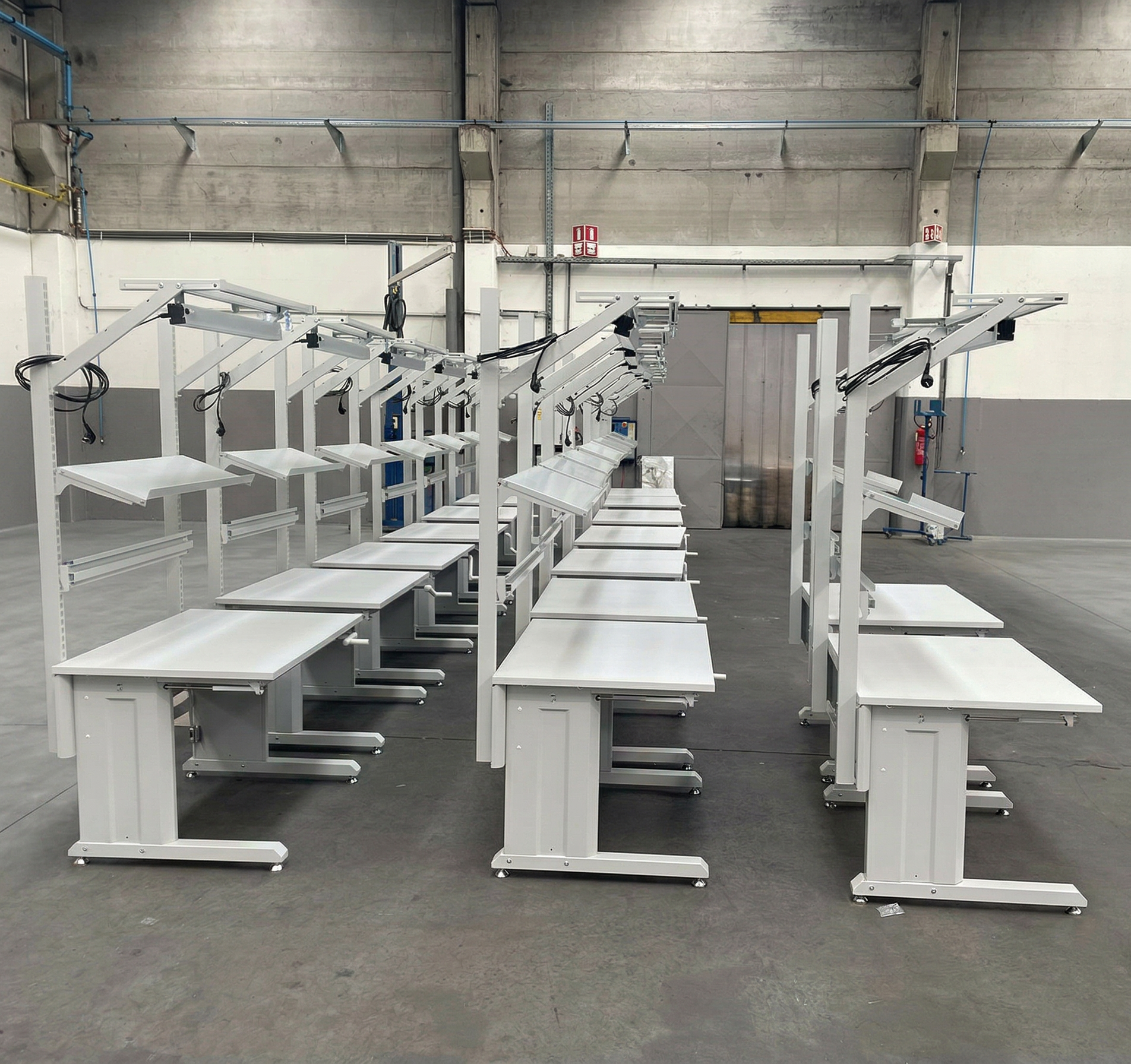 groot project van ergonomische werktafels met handzwengel uitgerust met bovenliggende draagstructuren en verlichting, klaar voor gebruik in een assemblage- of productieomgeving. grand projet de tables de travail ergonomiques avec manivelle équipées de structures de support en hauteur et d’éclairage, prêtes à être utilisées dans un environnement d’assemblage ou de production.