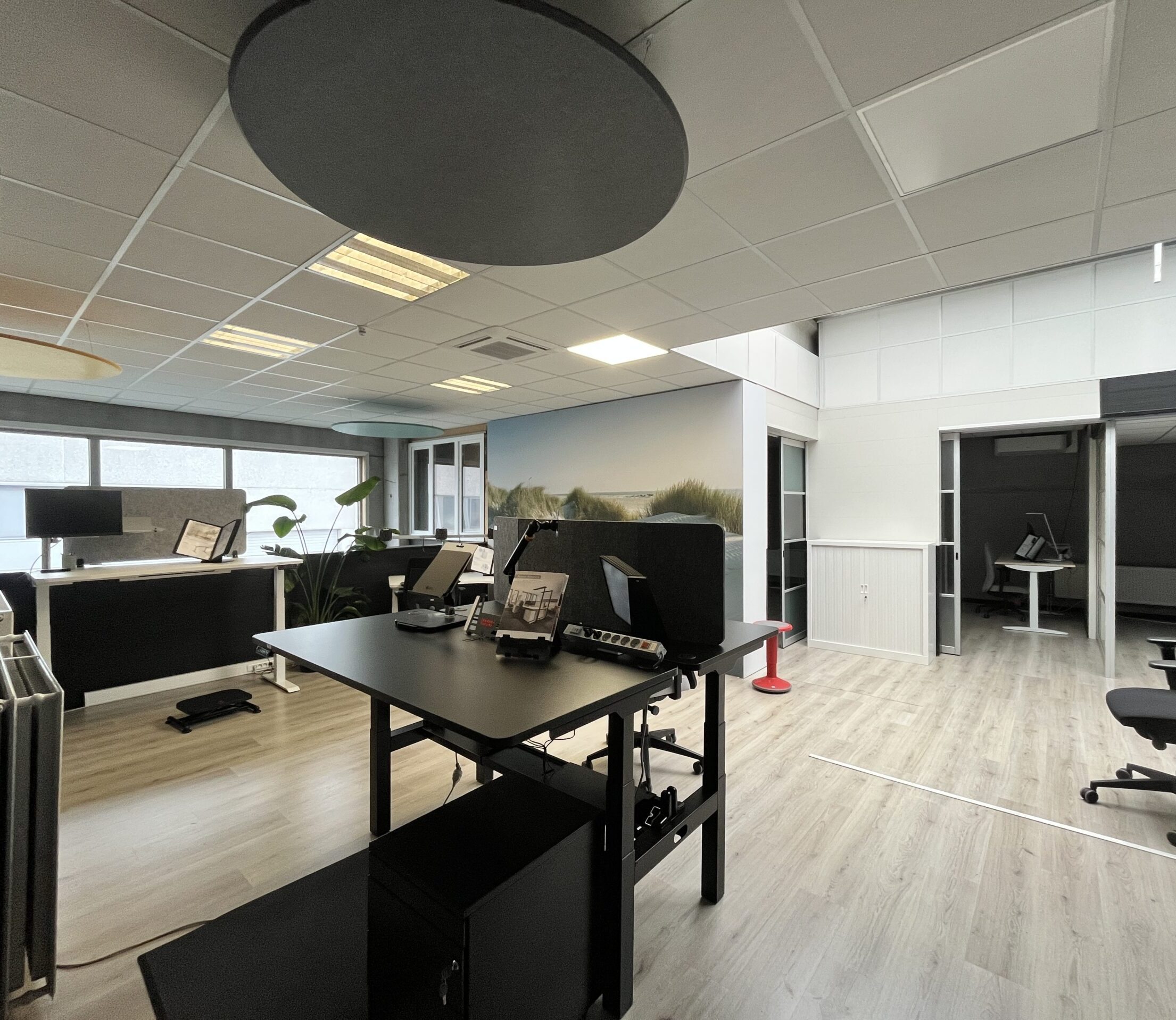 Overzicht van de AWP demoruimte met zwarte in hoogte verstelbare bureaus, grijze bureauscheidingswanden, glazen vergaderkamers op de achtergrond en diverse ergonomische bureauaccessoires