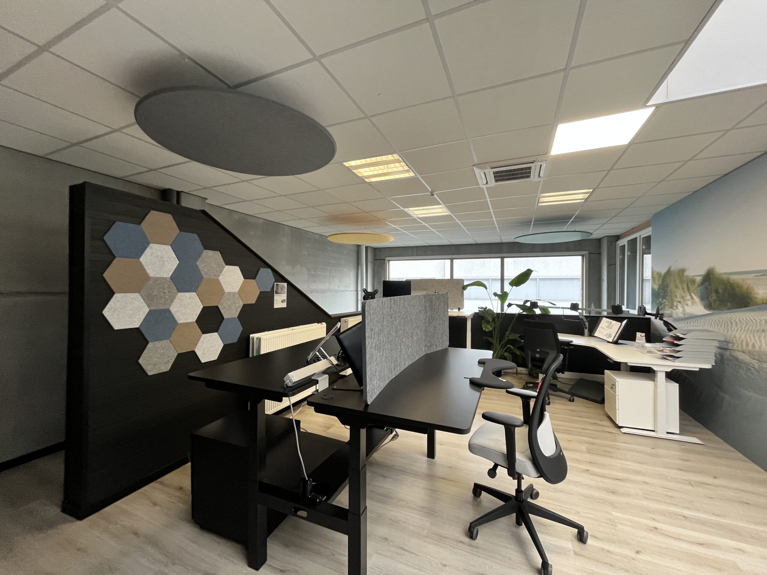 Modern kantoor in AWP demoruimte met zwarte en witte in hoogte verstelbare bureaus, ergonomische bureaustoelen, hexagonale akoestische wandpanelen en ronde plafondabsorbers