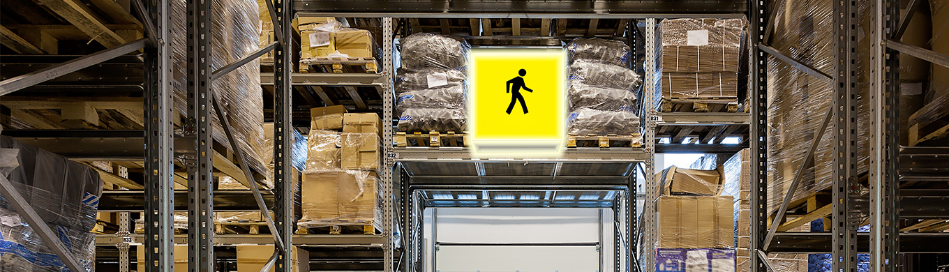Geel verlicht LED-bord met voetgangerspictogram tussen hoge palletrekken in een magazijn / Panneau LED jaune lumineux avec pictogramme piéton entre de hauts rayonnages à palettes dans un entrepôt