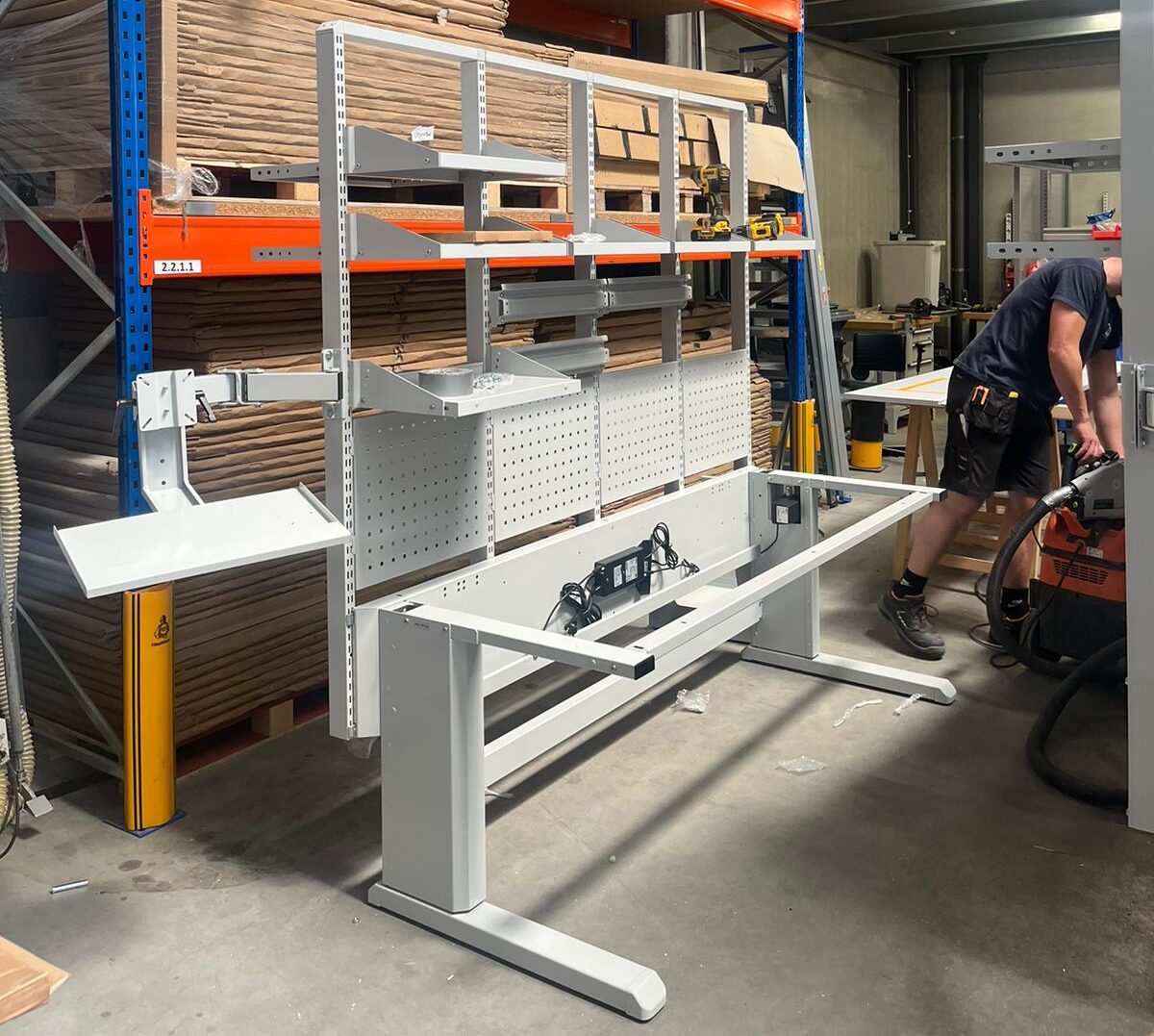 AWP technieker bouwt een in hoogte verstelbare industriële werktafel op in het atelier, met bovenstellingen en geperforeerde achterwand in aanbouw