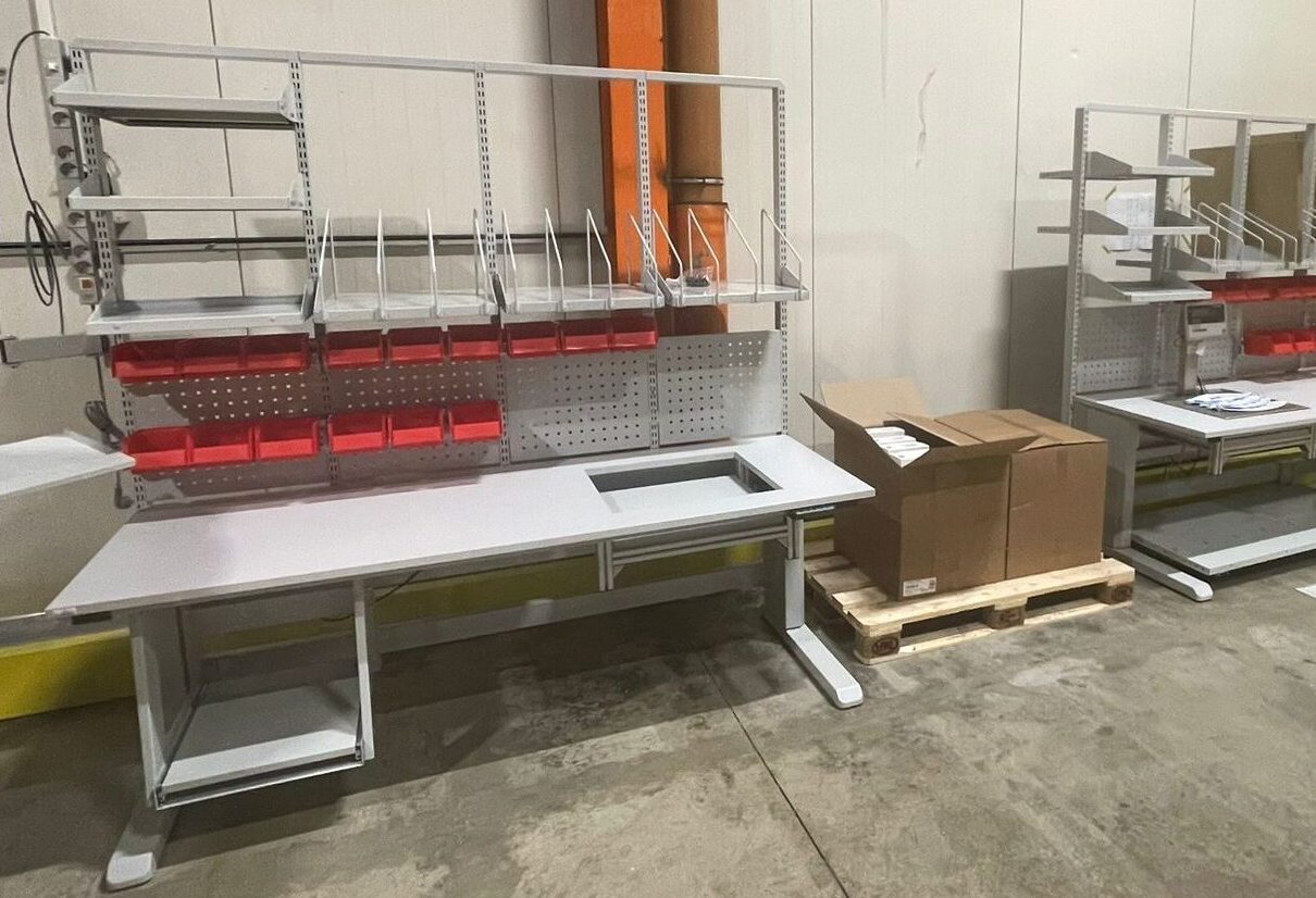 Twee volledig gemonteerde maatwerk werktafels met rode grijpbakken en bovenstellingen klaar voor levering in het AWP-atelier, met dozen producten op een pallet ertussen