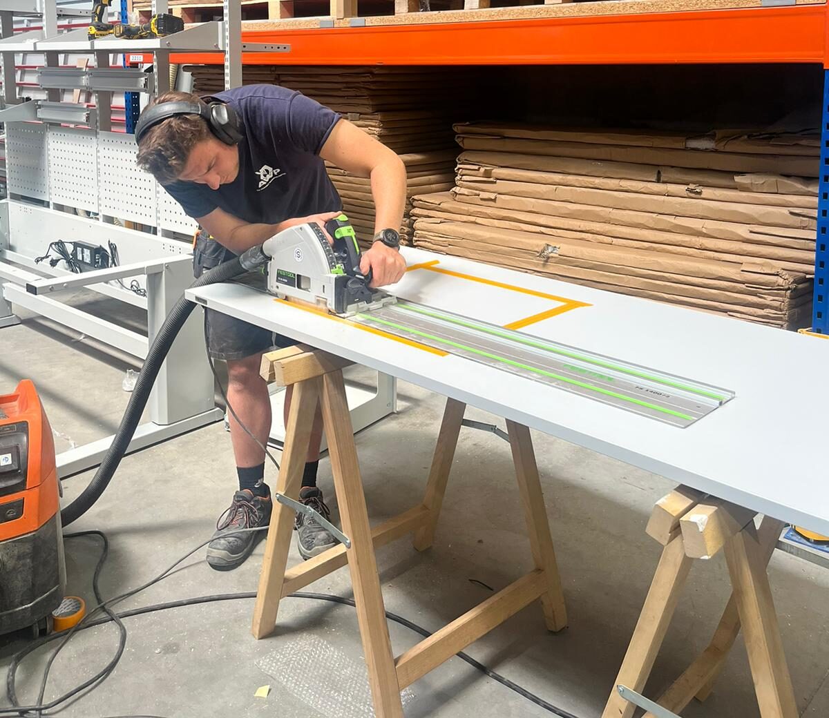 AWP-medewerker zaagt een wit tafelblad op maat met een geleiderailzaag en gehoorbescherming in het atelier