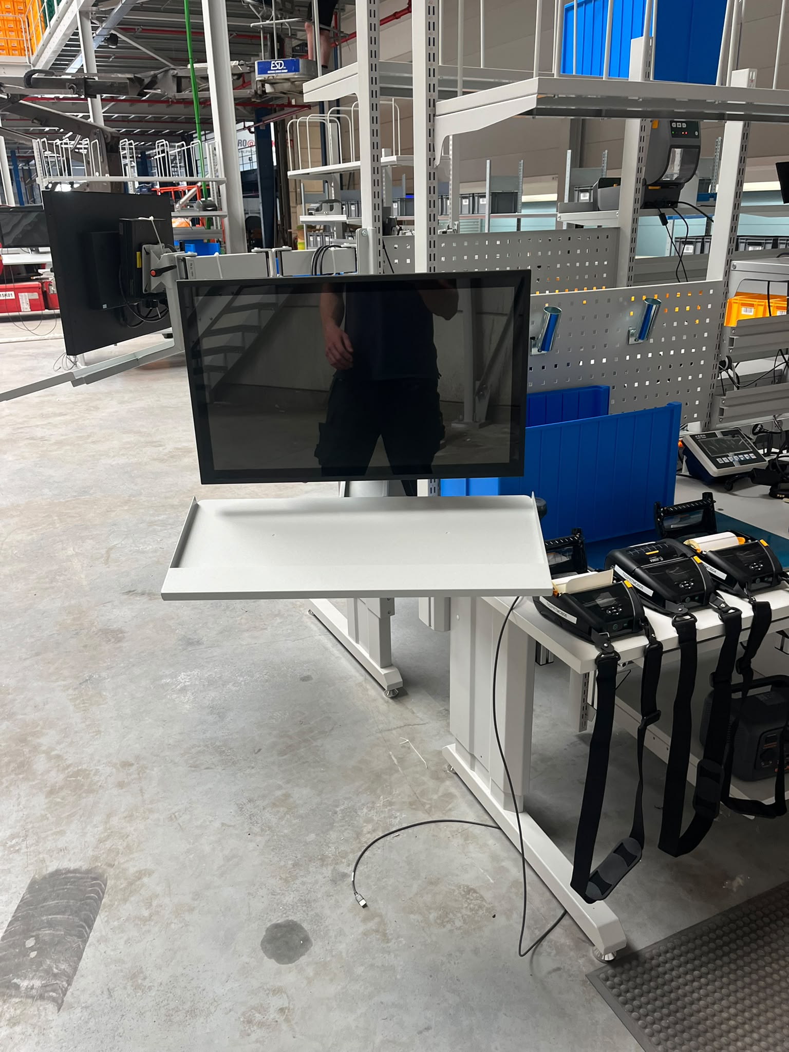 Monitorarm met scherm en toetsenbordhouder bevestigd aan een werktafel, onderdeel van de ergonomische werkpostinrichting in het magazijn van Pro@Work