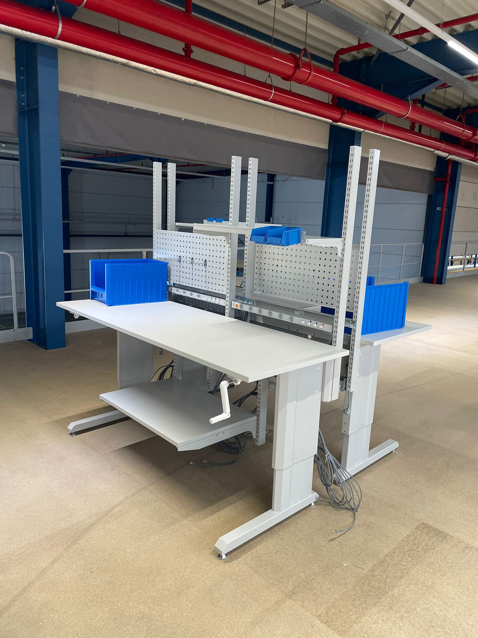Twee elektrisch hoogteverstelbere werktafels met prikbord en magazijnbakken als onderdeel van de ergonomische werkpostinrichting voor Pro@Work