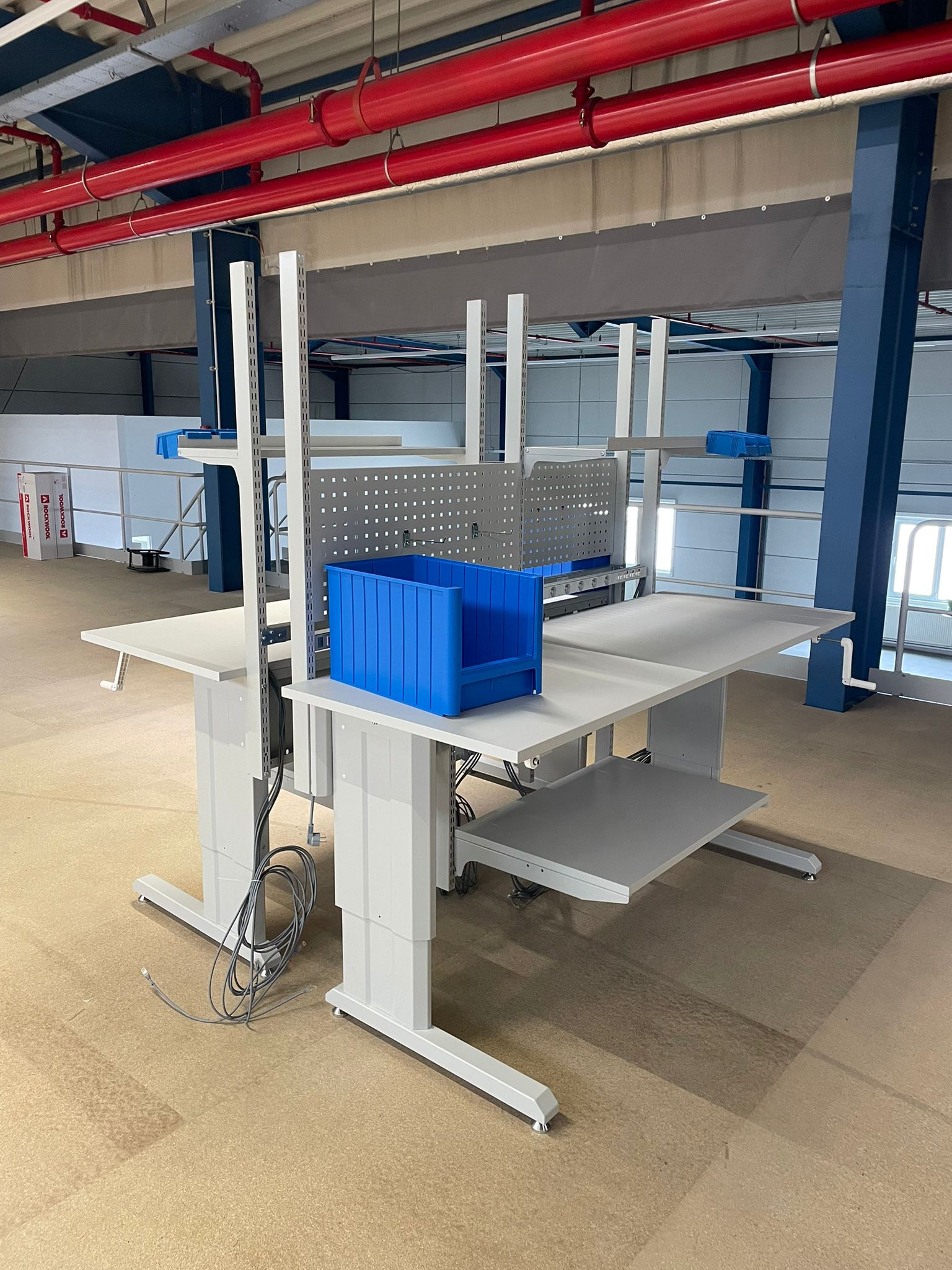 Schuine opstelling van meerdere werktafels met handzwengel als onderdeel van de ergonomische werkpostinrichting in het magazijn van Pro@Work