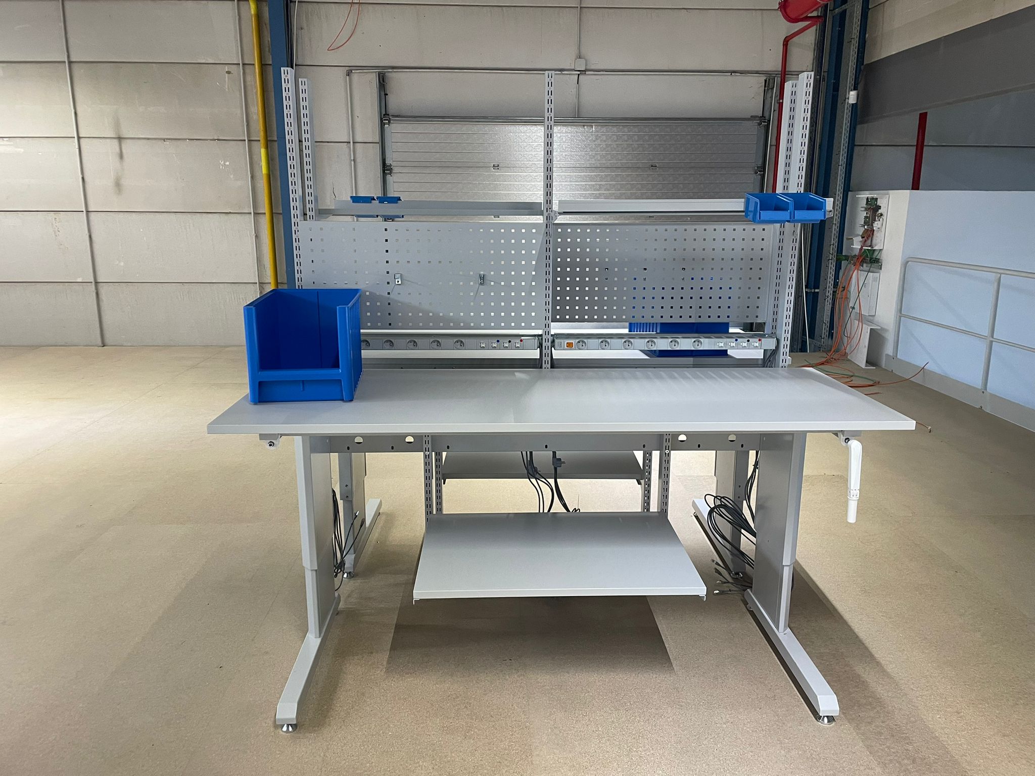 Dubbele in hoogte verstelbare werktafel met handzwengel, prikbord en stroomlat als onderdeel van de ergonomische werkpostinrichting voor Pro@Work