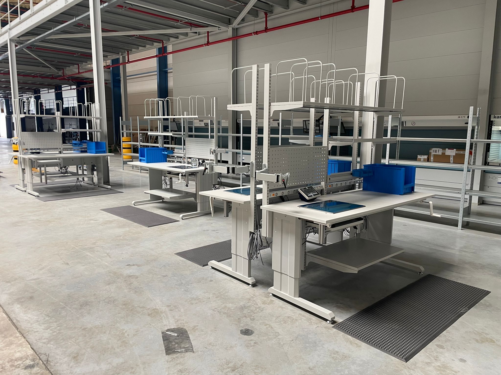 Rij van identieke ergonomische werkposten met antivermoeidheidsmatten in het nieuwe magazijn van Pro@Work, ingericht door AWP