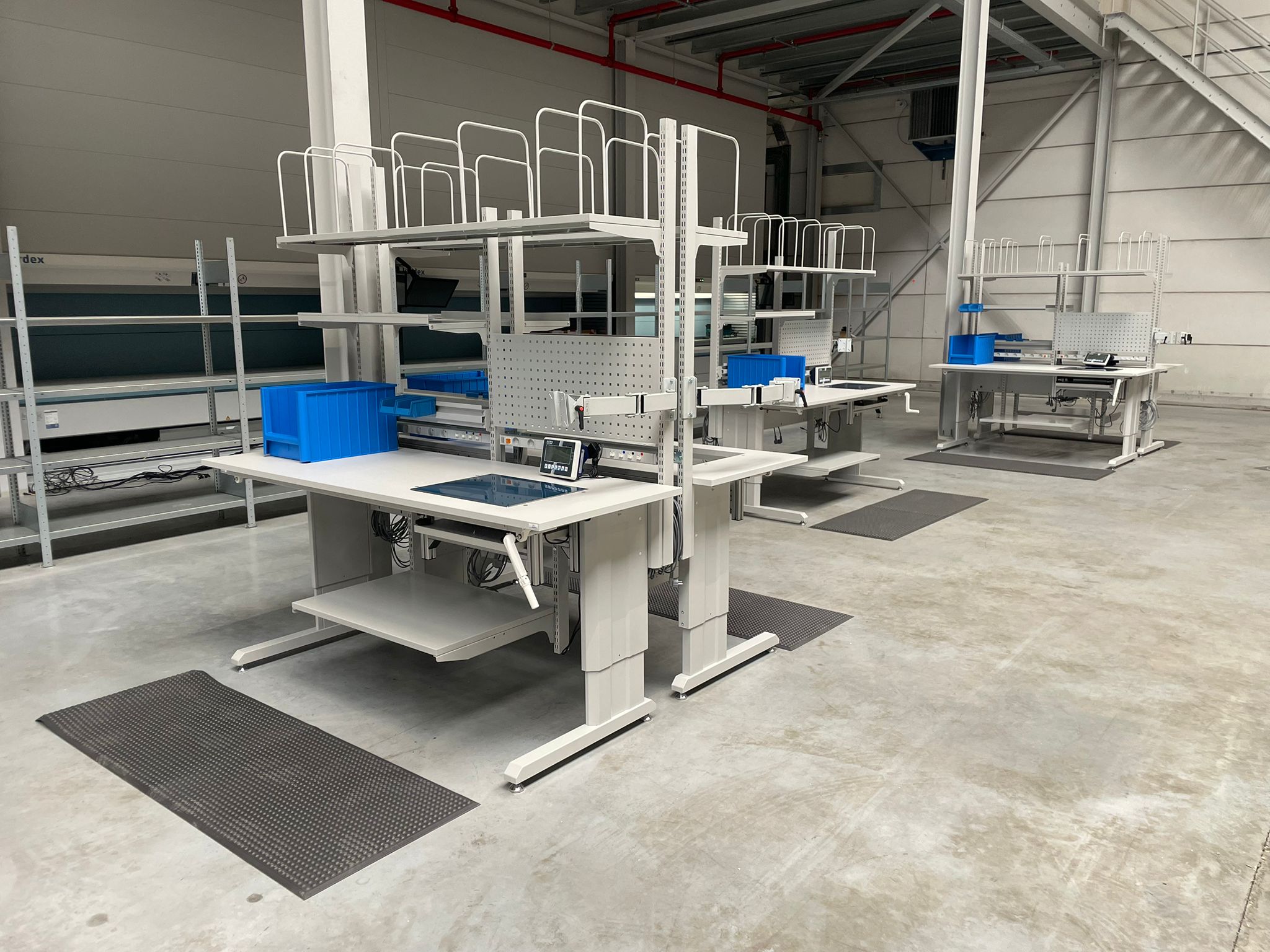 Meerdere elektrisch verstelbare ergonomische werkposten met antivermoeidheidsmatten en Kardex systemen op de achtergrond in het magazijn van Pro@Work