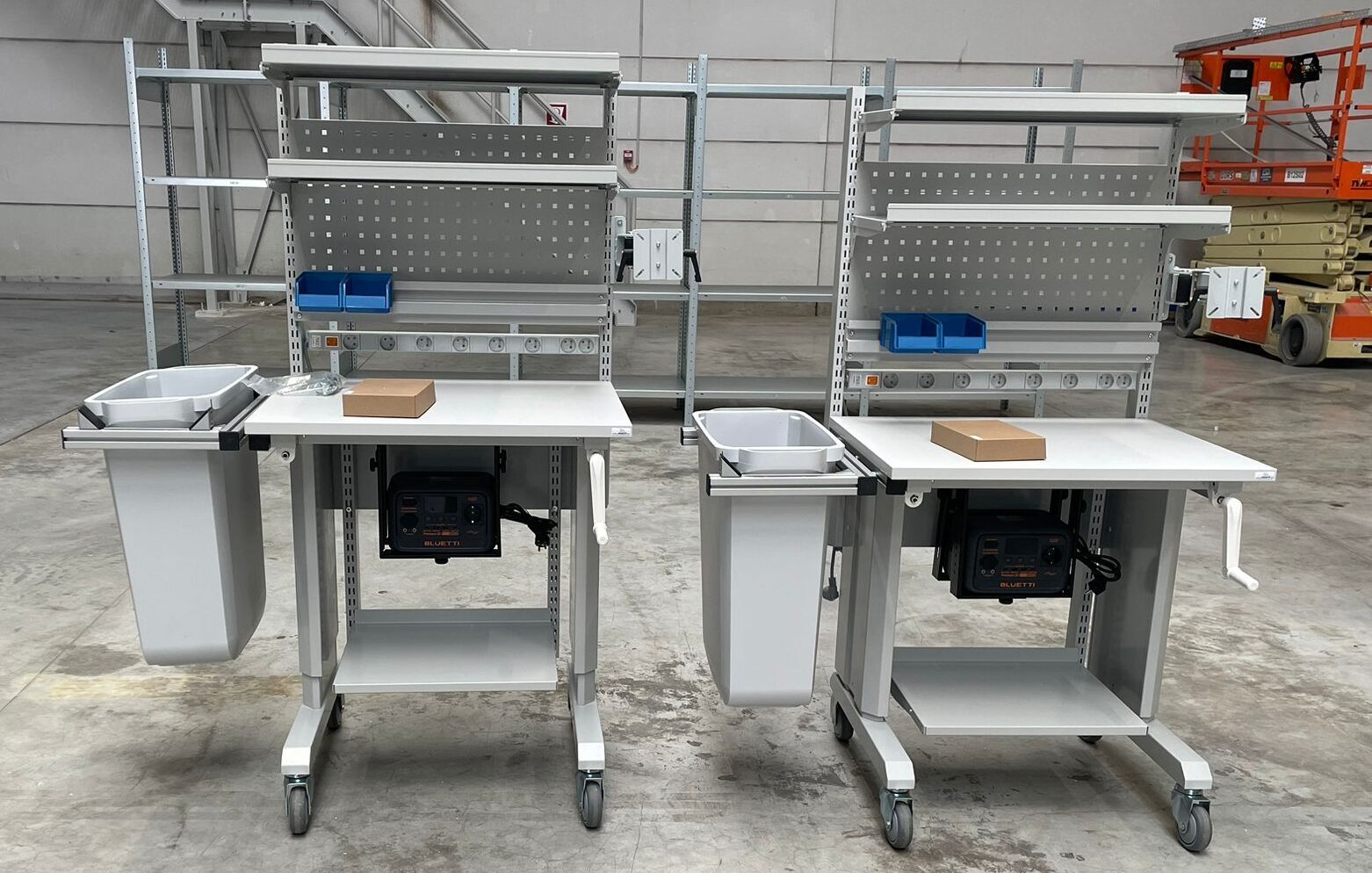 Twee identieke mobiele werktrolleys op wielen met handzwengel als onderdeel van de ergonomische werkpostinrichting in het magazijn van Pro@Work