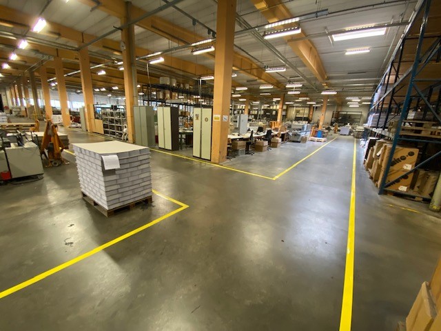 Gele vloerbelijning die opslagzones en rijdoorgangen markeert in de productieomgeving van Brepols