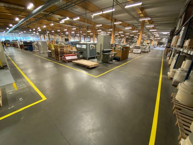 Gele vloerbelijning die rijroutes en zones afbakent in de productieomgeving van Brepols