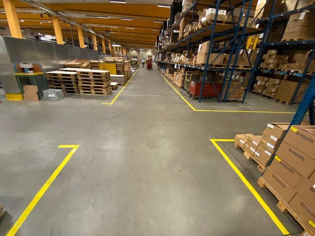 Gele vloermarkering aangebracht door AWP in de productieomgeving van Brepols voor duidelijke afbakening van zones en rijroutes