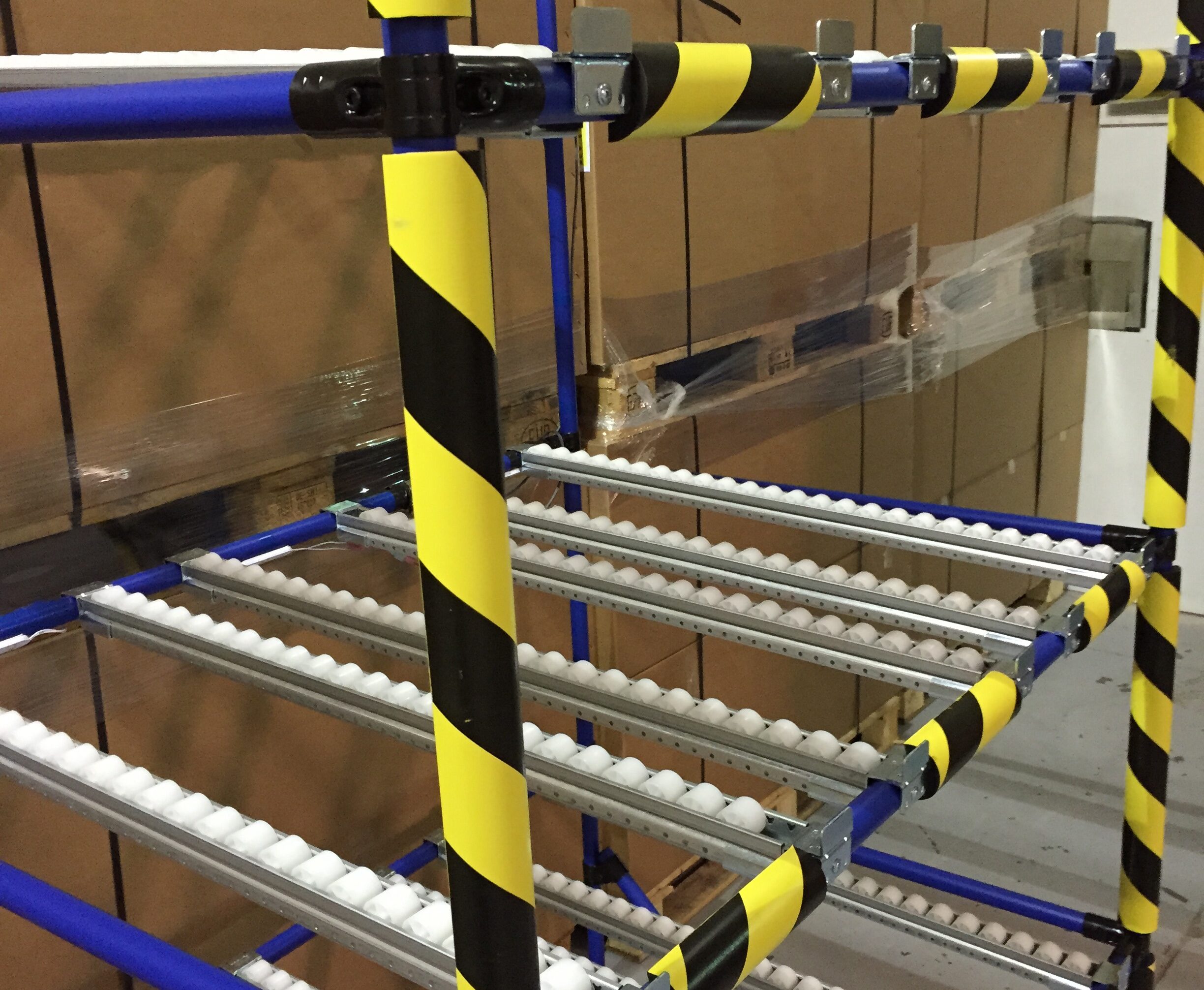 Zwart-gele bumper guards bevestigd op buizen en palen van een doorloopinstallatie met rollenband in een magazijn